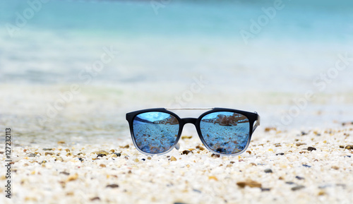 Fashion blue sunglasses on sandy beach near the blue sea. Summer holiday concept