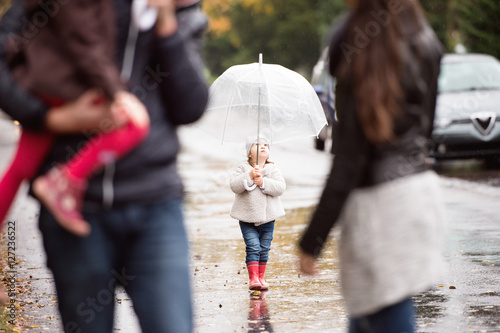 Little girl under the umbrella with her family, walking. Rainy d