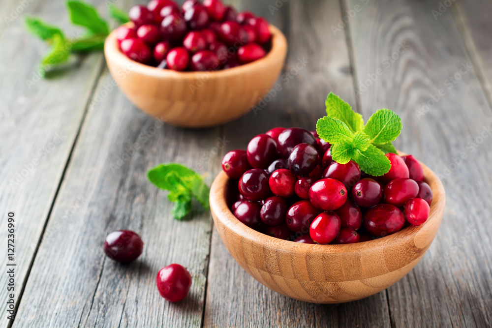 Fresh juicy cranberries in a bamboo bowl on the old wooden background. Selective focus. Fresh juicy cranberries in a bamboo bowl on the old wooden background. Selective focus.
