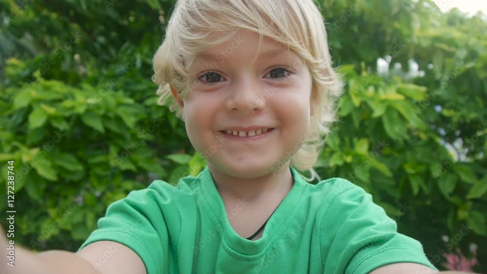 Wide angle view of smiling child video chats on smart phone on green tree background on windy day in park. Using a portable handheld device on summer vacation. Talking on a mobile. Doing selfie. Wide angle view of smiling child video chats on smart phone on green tree background on windy day in park. Using a portable handheld device on summer vacation. Talking on a mobile. Doing selfie.