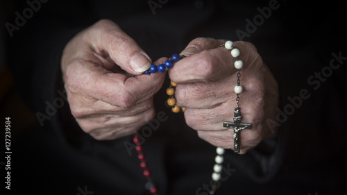 closeup of old female hands praying with rosary