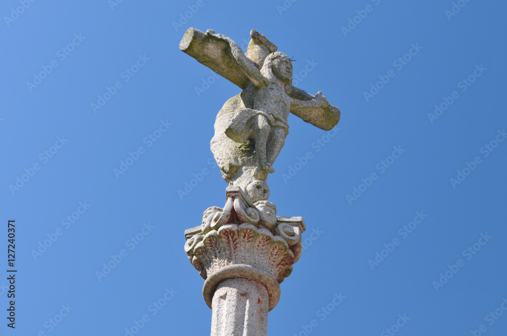 Kreuz mit Jesusfigur aus Stein vor blauem Himmel