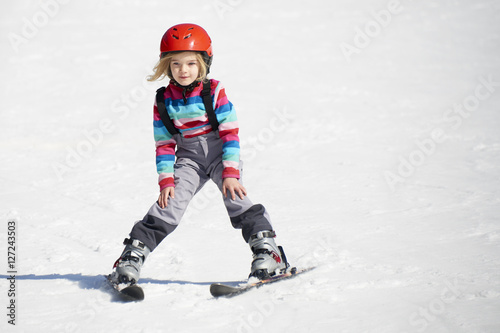 Happy child girl enjoying vacation in winter resort. Little girl skiing in mountains. Active sportive toddler wearing helmet learning to ski. Winter sport for family. Skier racing in snow.