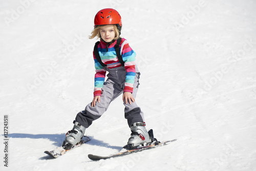 Happy child girl enjoying vacation in winter resort. Little girl skiing in mountains. Active sportive toddler wearing helmet learning to ski. Winter sport for family. Skier racing in snow. © Petr Bonek