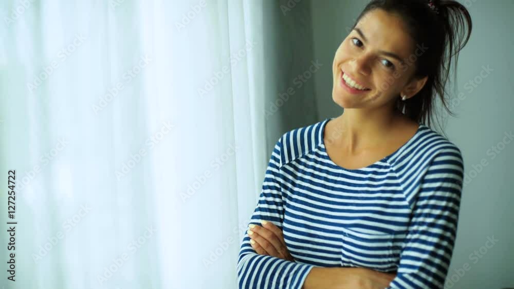 Smiling tanned beautiful lady staying near the window and posing on camera at home. Smiling tanned beautiful lady staying near the window and posing on camera at home.