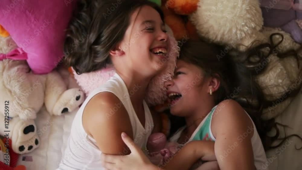 Two little angles are tickling each other in the bed completely covered with soft toys. Two little girls are tickling each other in the bed completely covered with soft toys. Childhood happiness. Two little angles are tickling each other in the bed completely covered with soft toys. Two little girls are tickling each other in the bed completely covered with soft toys. Childhood happiness.