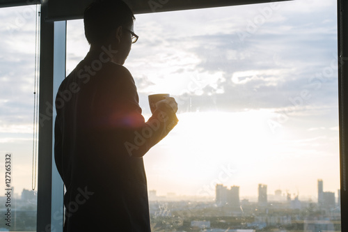 Silhouette of a businessman holding coffee and looking at city t