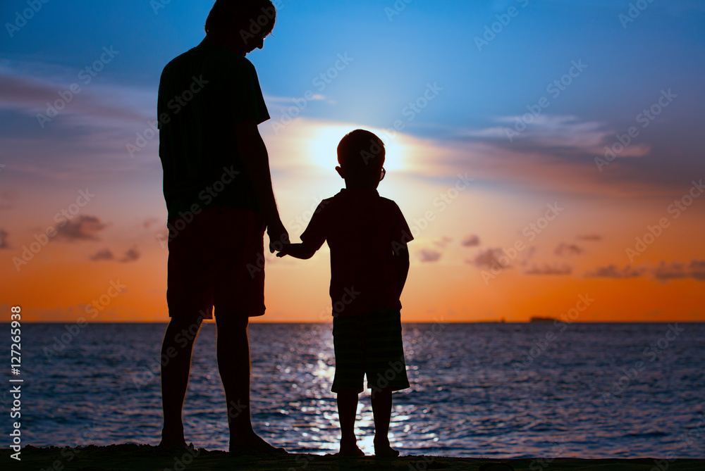 silhouettes of father and son holding hands at sunset