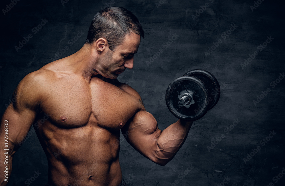 Shirtless middle age male holds dumbbell.