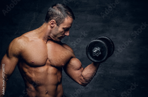 Shirtless middle age male holds dumbbell.