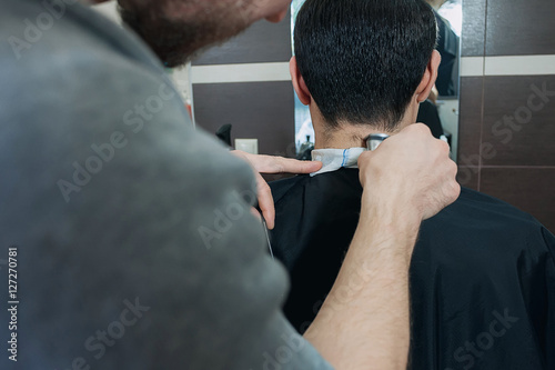Master hairdresser cutting a short cut young man in barber shop. dark-haired client in bright cape sitting on the chair at barbershop.