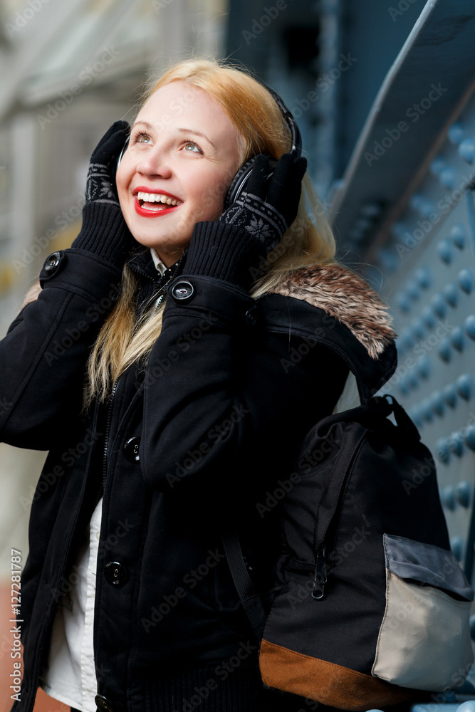 Fototapeta premium Cheerful ginger girl with headphones listening music at blue wall