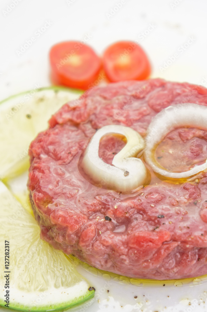 Steak tartare closeup with lemon slices on white plate Steak tartare closeup with lemon slices on white plate