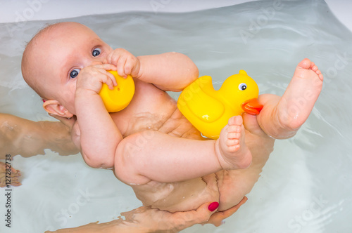 Fototapeta Newborn baby girl bathing and playing with rubber duck