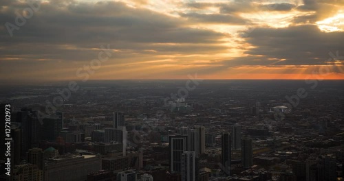 Chicago, Illinois, USA - view from top of the John Hancock Center of the City with United Center and railway at sunset with clouds, sunbeams and orange sky - Timelapse with zoom in