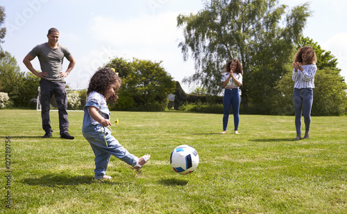 Mum and friends watch her daughter kicking a ball outdoors © Monkey Business