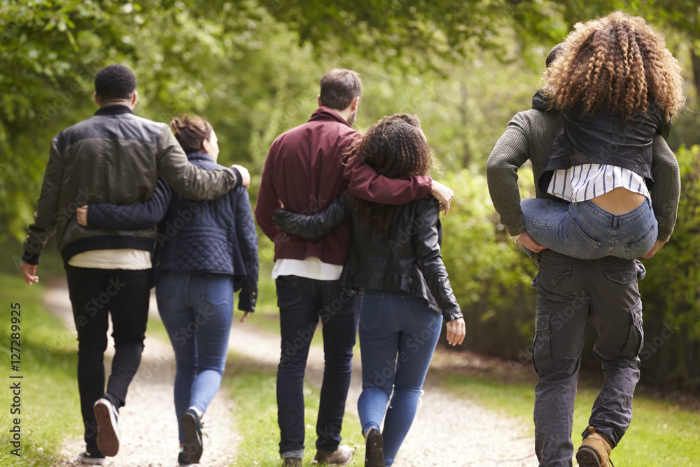 Young couples walk and piggyback in country lane, back view Young couples walk and piggyback in country lane, back view