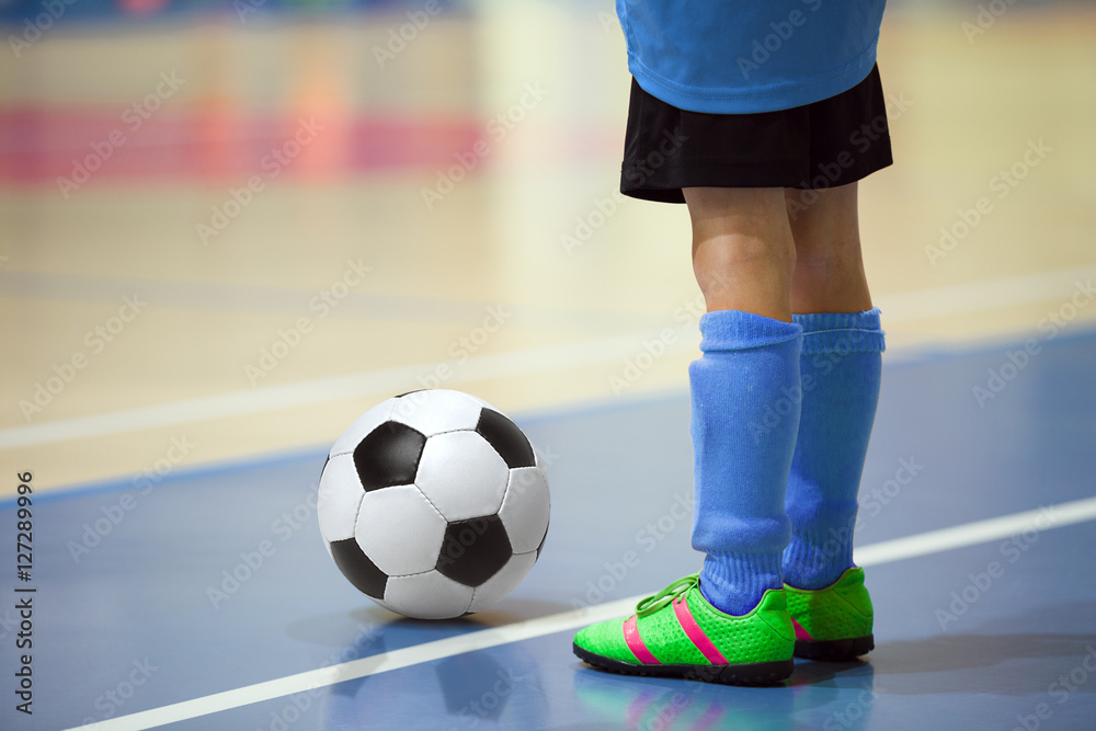 Fototapeta premium Football futsal training for children. Indoor soccer young player with a soccer ball in a sports hall. Player in blue uniform. Sport background.