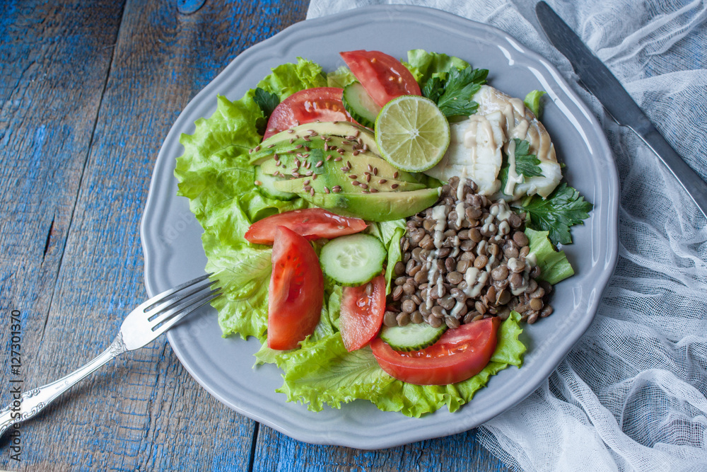 Healthy green salad with boiled cod fish, lentils, tahini, parsley, tomatoes, cucumbers, avocados, flax seeds on a large gray plate. Love for a healthy raw food concept Healthy green salad with boiled cod fish, lentils, tahini, parsley, tomatoes, cucumbers, avocados, flax seeds on a large gray plate. Love for a healthy raw food concept