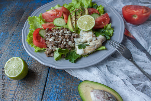 Healthy green salad with boiled cod fish, lentils, tahini, parsley, tomatoes, cucumbers, avocados, flax seeds on a large gray plate. Love for a healthy raw food concept