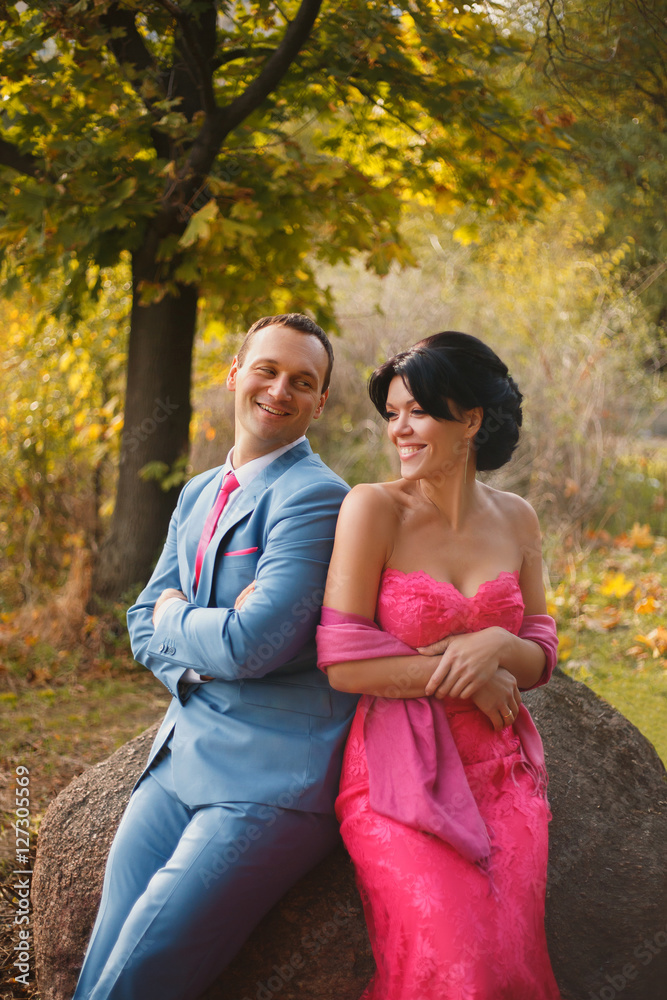 Happy couple, they smile sitting on a large stone, shoulder in shoulder. Happy couple, they smile sitting on a large stone, shoulder in shoulder.