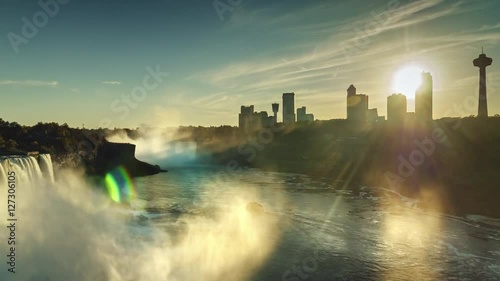 Epic sunset in the Niagara River. The rays of the setting sun shining through the silhouettes of skyscrapers on the Canadian side of the river. The camera pans to Niagara Falls. The sun's rays shine photo