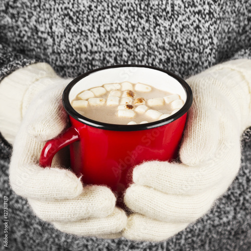 Girl keeps a mug of hot cocoa with marshmallows in mittens