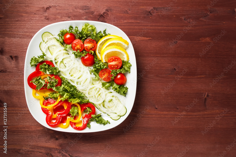 Salad with tomatoes, cucumbers, sweet peppers and onions on a square plate on a wooden table