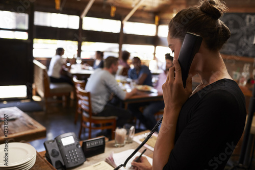 Young woman taking a reservation by phone at a restaurant