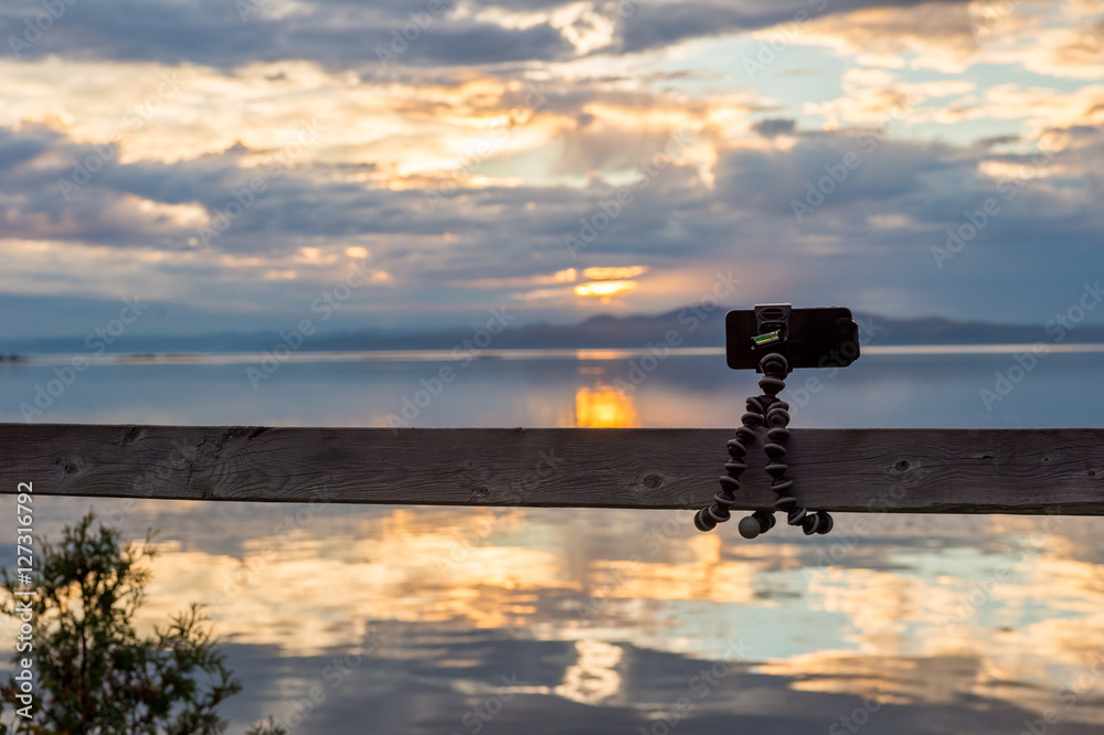 Obraz premium Smartphone attached on flexible tripod facing the sea at sunset