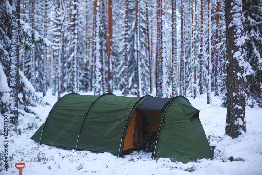 A process of camping in winter forest, setting a tent covered in snow, making a bonfire campfire and cooking food with portable gas cooker and fire, snowy landscape
