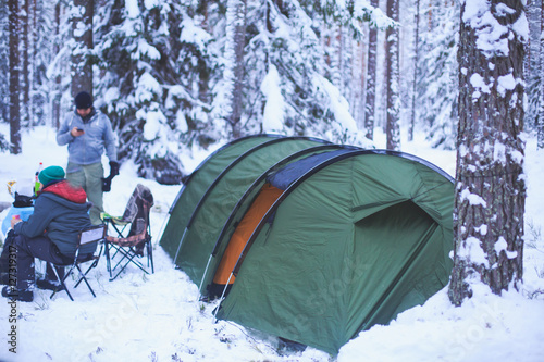 A process of camping in winter forest, setting a tent covered in snow, making a bonfire campfire and cooking food with portable gas cooker and fire, snowy landscape 
