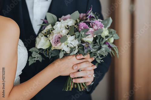Bride and groom standing side by side and holding a wedding bouquet of white flowers, pink flowers and greenery