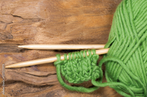 Green wool with knitting needles lying on wood