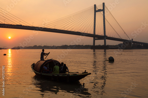 Wooden boat on river Hooghly at sunset with Vidyasagar bridge at the backdrop (silhouette), These country boats are used for pleasure boat rides on the river. photo