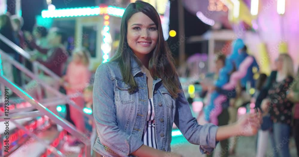 Laughing woman relaxing at a fairground standing in a brightly lit stall with pink strip lights grinning happily at the camera Laughing woman relaxing at a fairground standing in a brightly lit stall with pink strip lights grinning happily at the camera