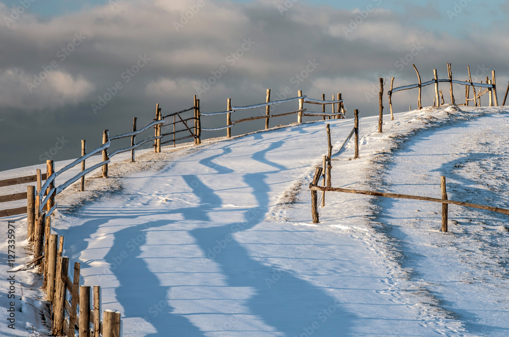 Fototapeta premium Fence pastures on a hill at sunset against the sky. A fabulous winter landscape.