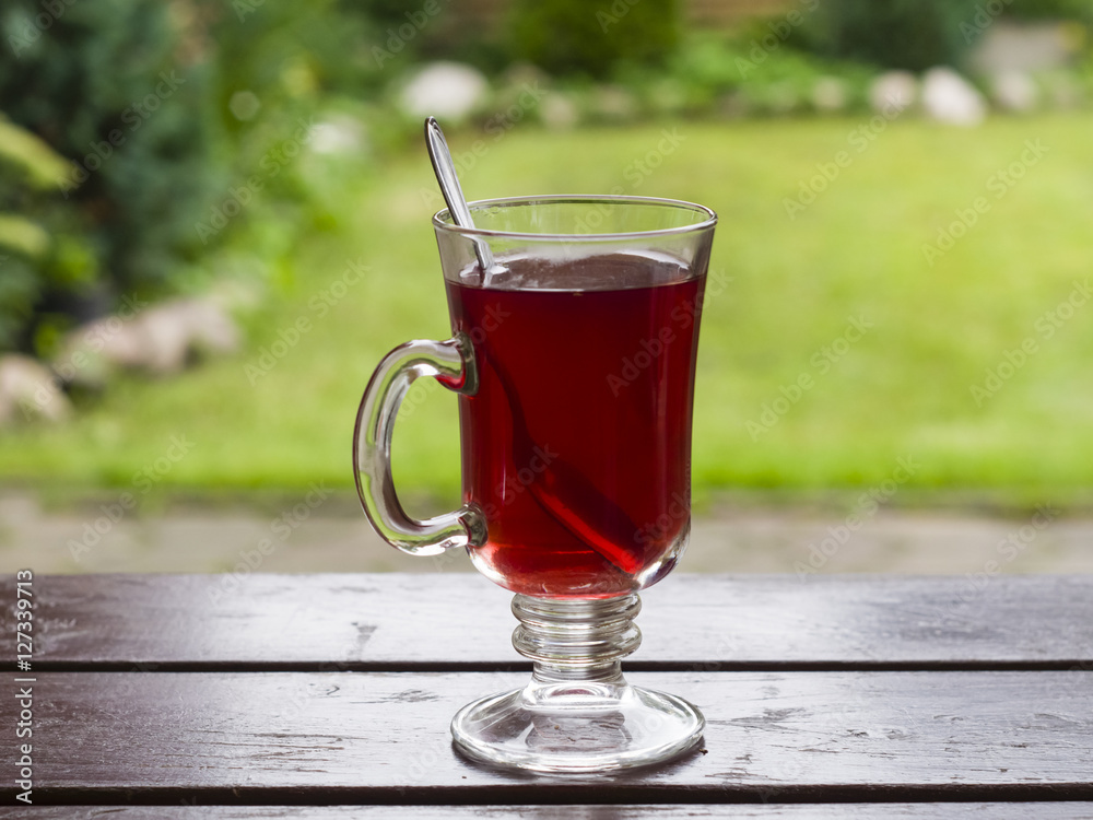 Red fruit tea in glass cup with spoon on wooden table, bokeh background, selective focus, shallow DOF Red fruit tea in glass cup with spoon on wooden table, bokeh background, selective focus, shallow DOF