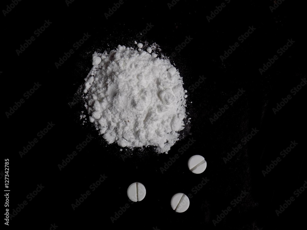 Cocaine drug powder pile and pills on black background