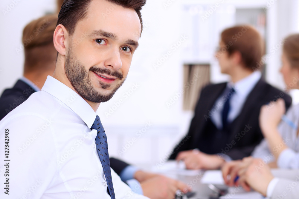 Portrait of cheerful smiling businessman against a group of people at meeting. Portrait of cheerful smiling businessman against a group of people at meeting.