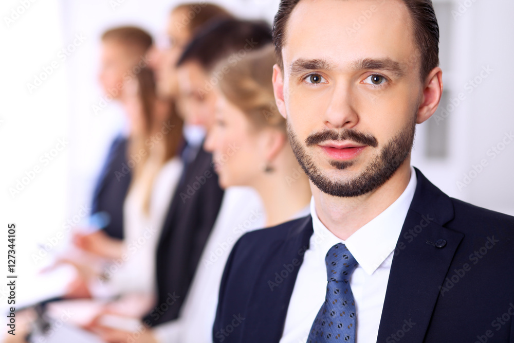 Portrait of cheerful smiling businessman against a group of people at meeting. Portrait of cheerful smiling businessman against a group of people at meeting.