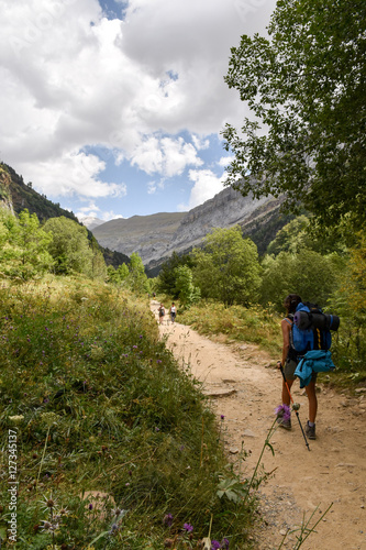 Girl with backpack and walking sticks strolling down a mountain