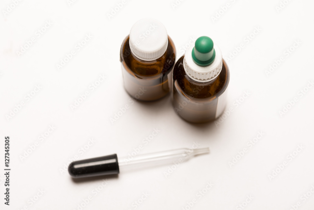 Studio image of clear glass pipette arranged with brown medicinal bottles against white background with soft shadows