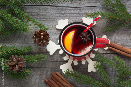 Christmas and festive mulled wine in a red mug with spices, cinnamon, star anise, cone, fir branch on a rustic wooden table. Christmas composition. Top view. photo