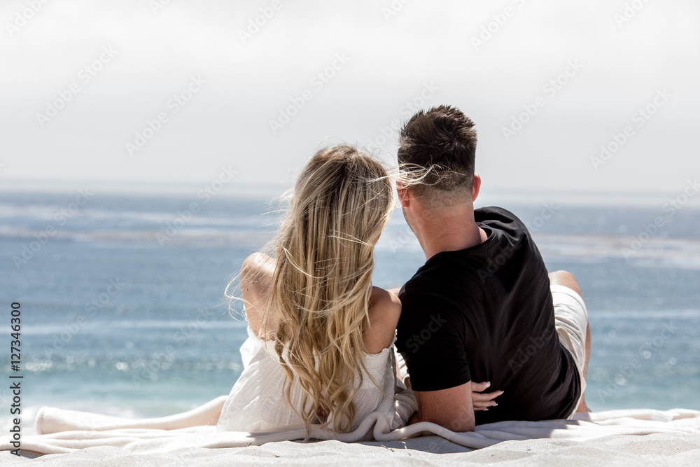 Lovely couple hugging on the beach and looking at the ocean on a sunny day