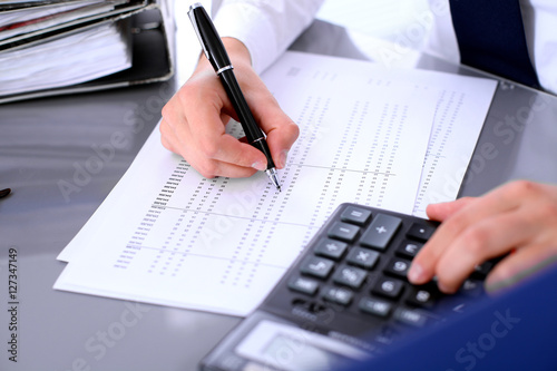 Bookkeeper or female financial inspector making report, calculating or checking balance. Internal Revenue Service checking financial document. Audit concept.