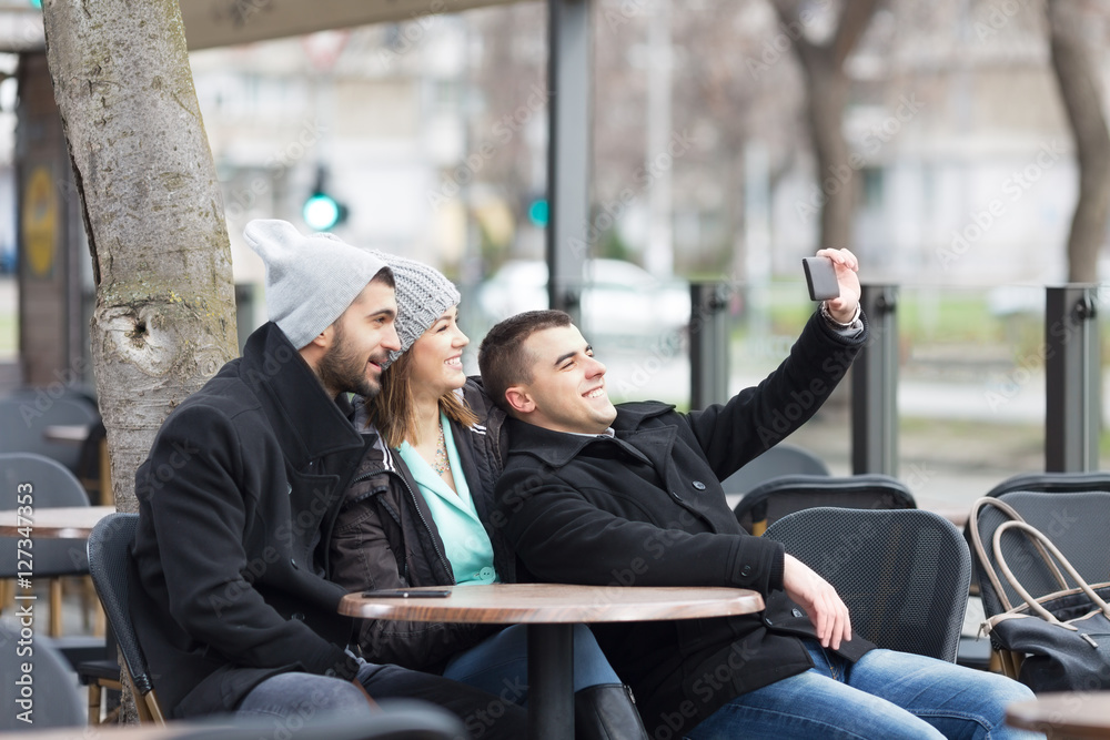 Group of young friends is sitting in an outdoor caffe and makeing a selfie.