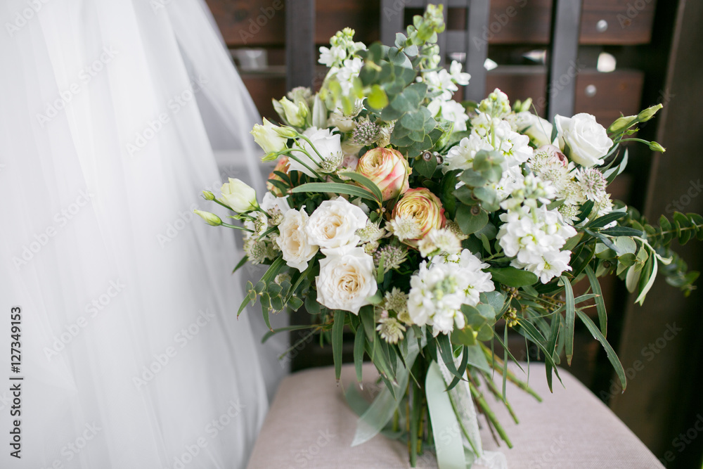 Bridal bouquet. The bride's . Beautiful of white flowers and greenery, decorated with silk ribbon, lies on vintage wooden chair Bridal bouquet. The bride's . Beautiful of white flowers and greenery, decorated with silk ribbon, lies on vintage wooden chair