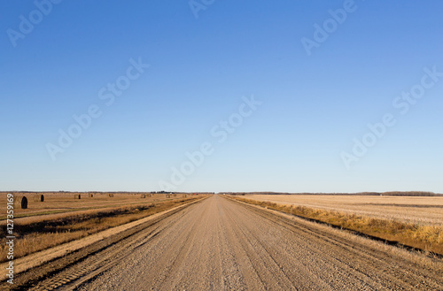 Gravel road dividing harvested fields and round straw bales in rural countryside autumn landscape