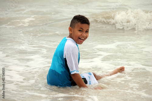 Young Biracial Boy Sitting in the Ocean and Smiling